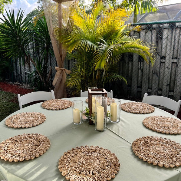 Outdoor table setting with decorative placemats and candles under a canopy.