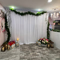 Decorative setup with white fabric, flowers, and candles on a stone floor.