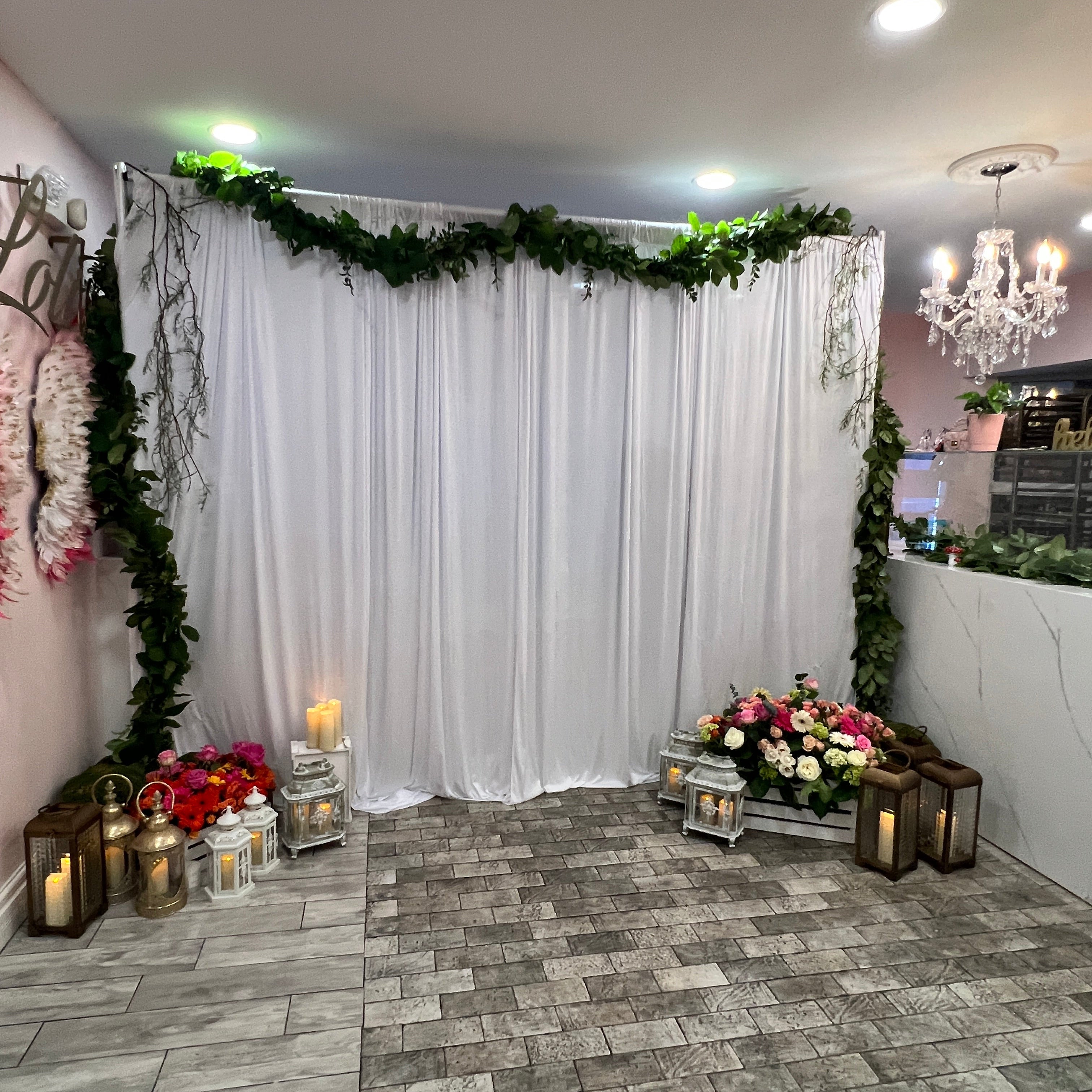 Decorative setup with white fabric, flowers, and candles on a stone floor.