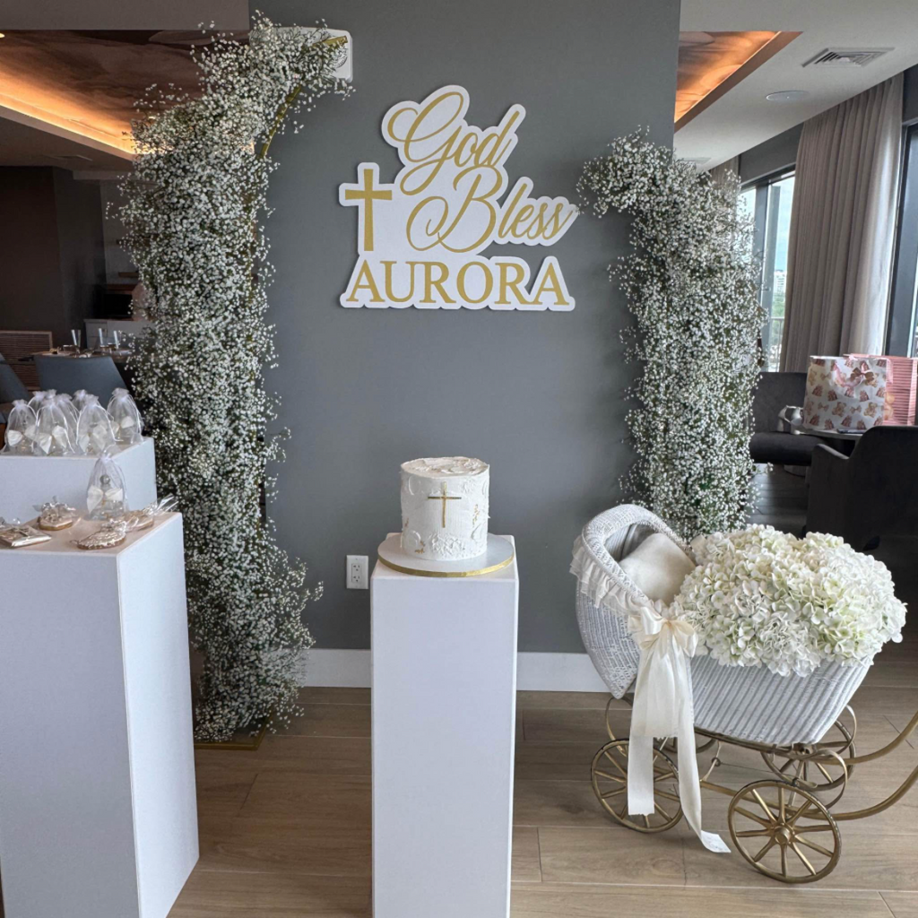 Decorated room with floral arrangements, a cake, and a sign on a gray wall.
