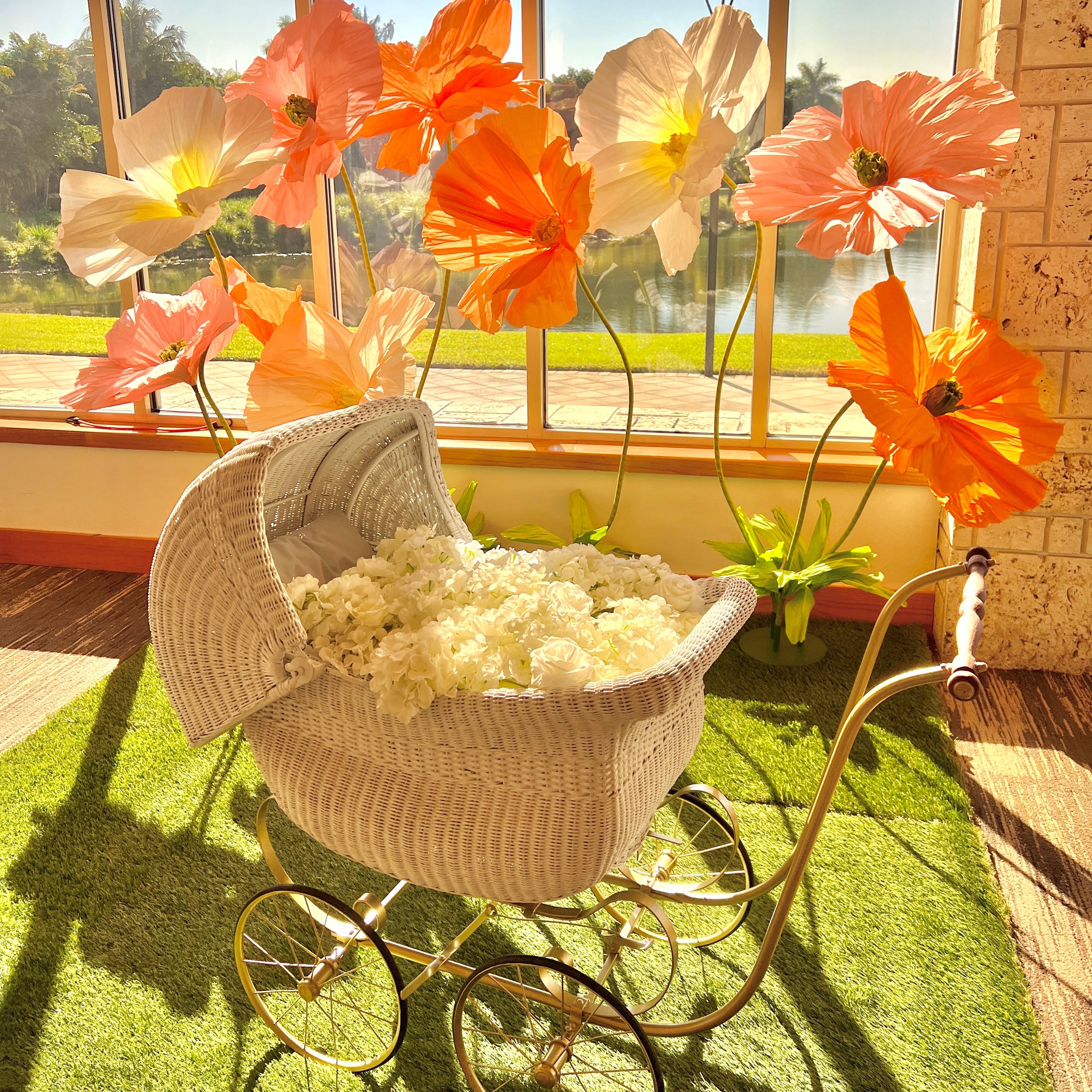 Vintage-style baby carriage with large decorative flowers in a sunroom. 