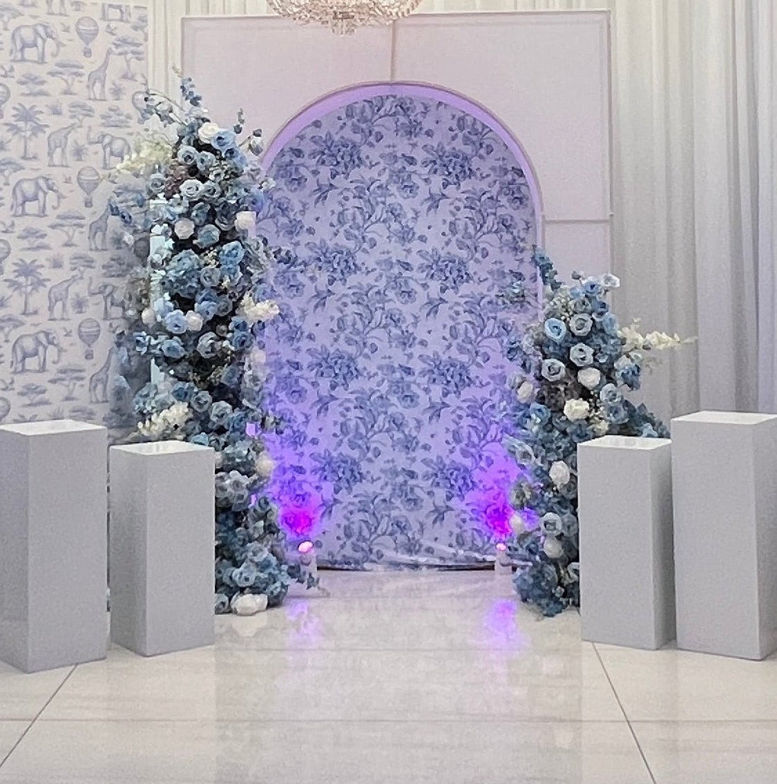 Decorative setup with floral arch, chandelier, and floral arrangements in a room.