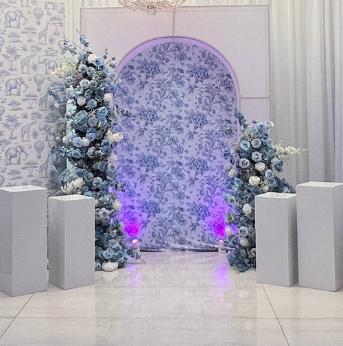 Decorative setup with floral arch, chandelier, and floral arrangements in a room.