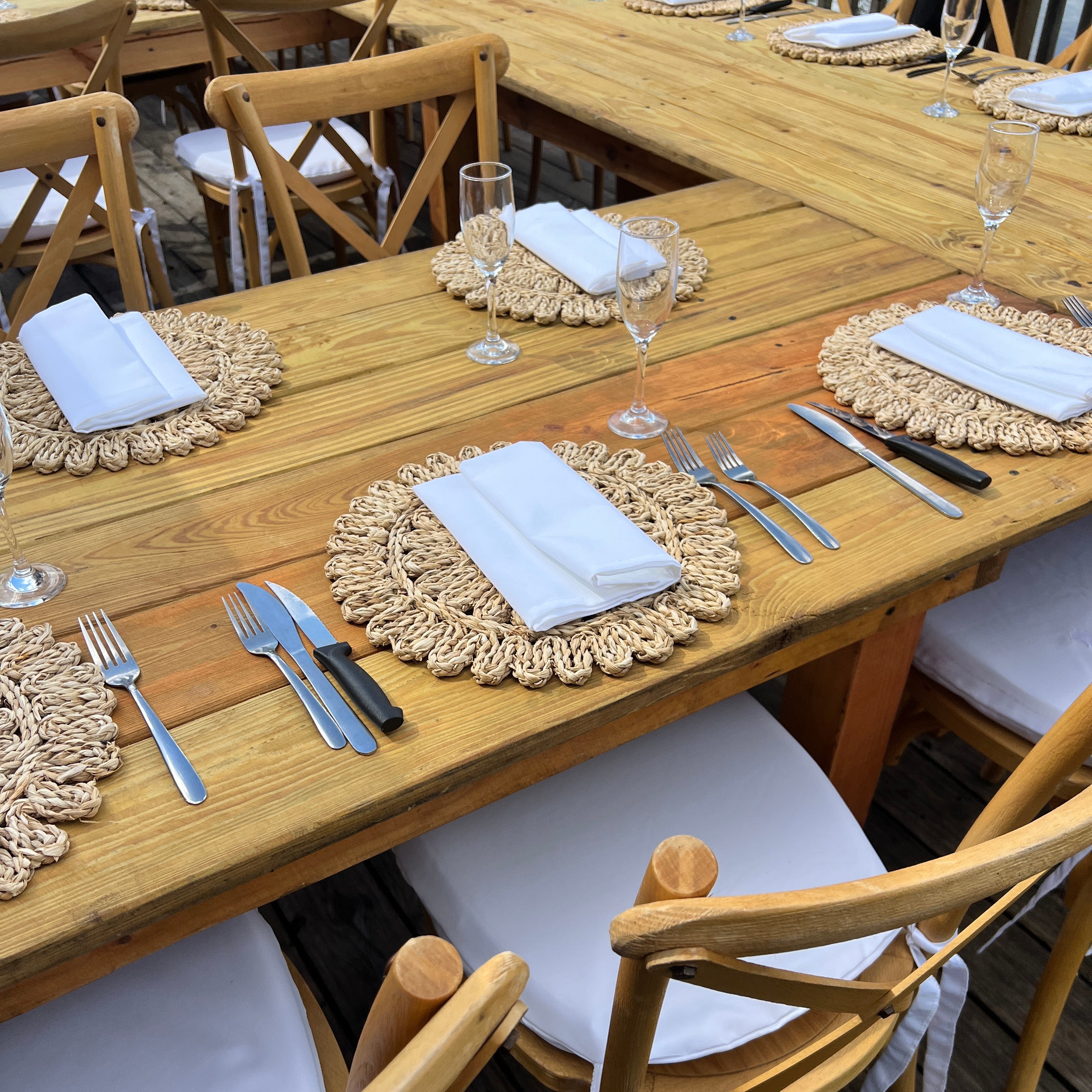 Dining table set with chairs, place mats, and cutlery on a wooden deck.