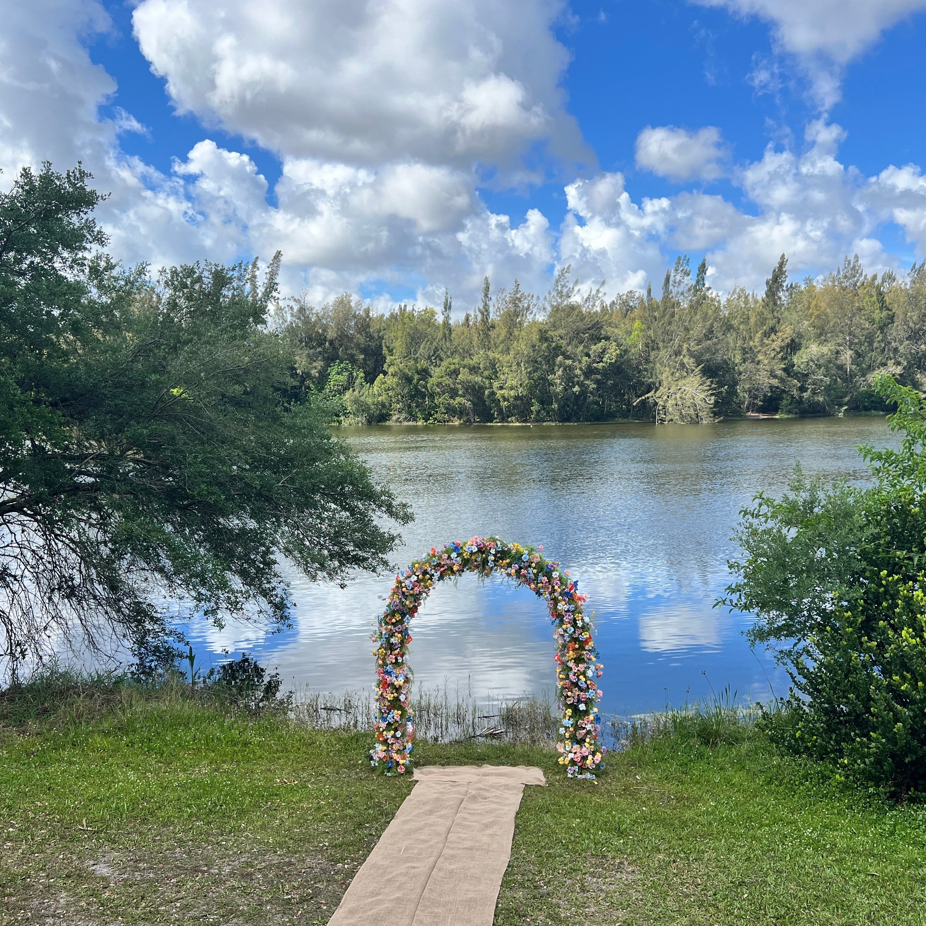 Floral archway by a lake with trees and blue sky in the background